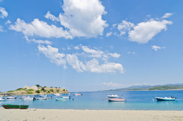 Fototapeta na wymiar Under the perfect clouds, boats in a small fishing harbour at the beach in Sithonia, Greece
