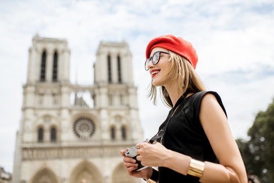 Young woman tourist in red cap standing with photo camera in front of the famous Notre Dame cathedral in Paris