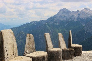 Some wooden chairs for visitors, made out of tree trunks, and a panoramic view of the mountains. On the terrace of a mountain hut. Theth national park, North Albania, Southeast Europe.