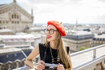 Young woman tourist in red cap standing with photocamera on the terrace with great cityscape view...