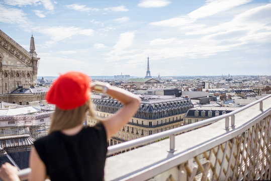 Young woman in red cap standing on the terrace with great cityscape view with Eiffel tower in Paris. Woman is out of focus