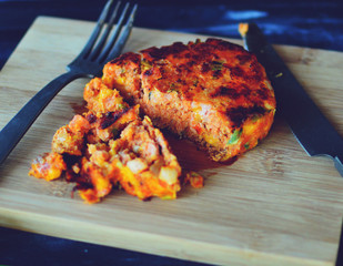 Salmon burger on wood platter with eating utensils.  Delicious gourmet dinner.