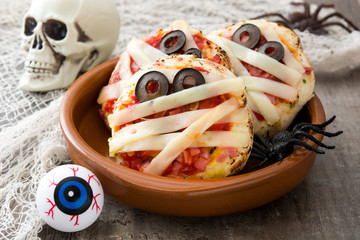 Halloween mummies mini pizzas on wooden table.
