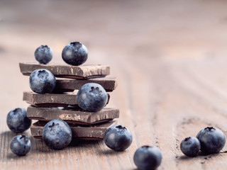 Stack of dark chocolate and fresh ripe blueberries. Blueberry and chocolate on wooden background. Copy space.