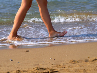 man's feet walking barefoot on beach by water edge