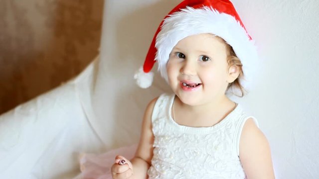 Happy Child adorable girl in Santa hat smilling sits near a Christmas