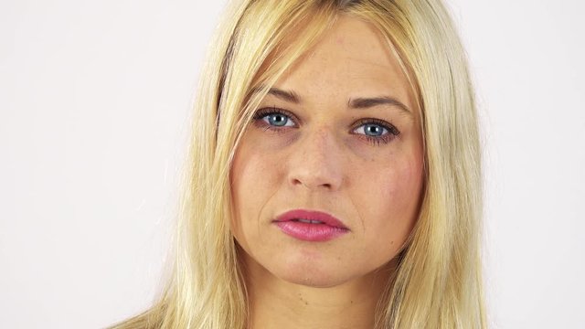A young attractive woman looks seriously at the camera - face closeup - white screen studio
