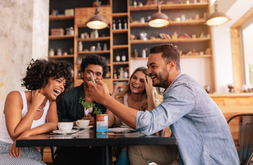 Happy young group of friends using mobile phone at cafe
