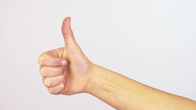 A woman shows a thumb up to the camera - closeup on the hand - white screen background