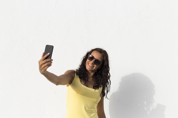 Naklejka premium young woman taking a selfie with mobile phone over white background. sunny. summer. lifestyle