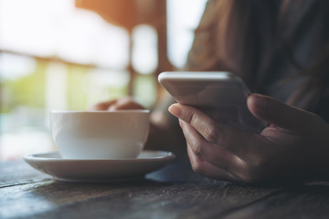 Closeup image of a woman using and looking at smart phone while holding a white coffee cup in...