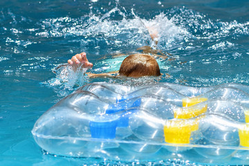 Young caucasian red hair boy swimming in a blue waterpool with yellow blue inflatable air mattress,...