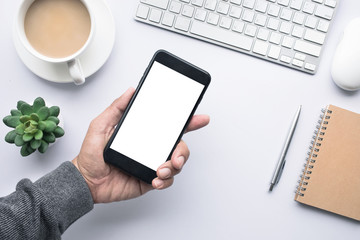 Male hand holding smartphone on office desk table with copy space in white background.flat lay