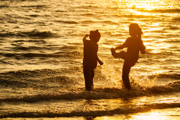 Silhouette of young girls kicking splash water on the beach at sunset.