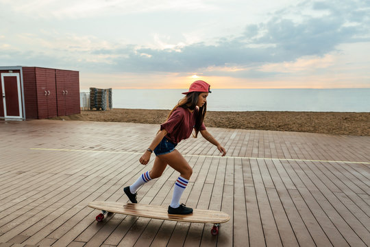 Trendy girl riding a longboard by the beach at sunrise.
