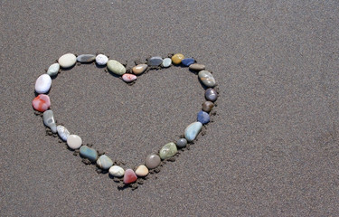 colored pebbles collected in the form of heart on the sea sand