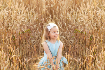 Little girl on a gold wheat field walking in the sunset. Happy four years old girl smiling and laughing in summer day at nature