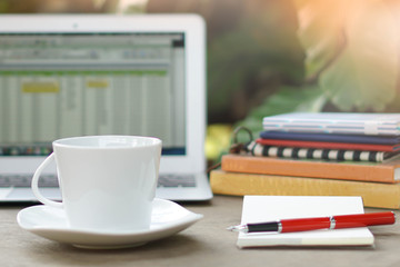 Laptop spread sheet, coffee cup, books and notebook blank page with red pen on business desk business garden background concept