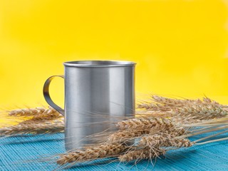 wheat spikelets and metal mug on bamboo mat. yellow background