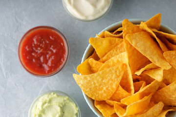 Nachos or tortilla in bowl with dipping sauces on gray background.