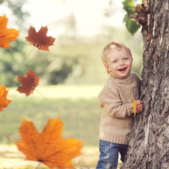 Autumn portrait of happy child playing having fun with flying yellow maple leaves, wearing sweater