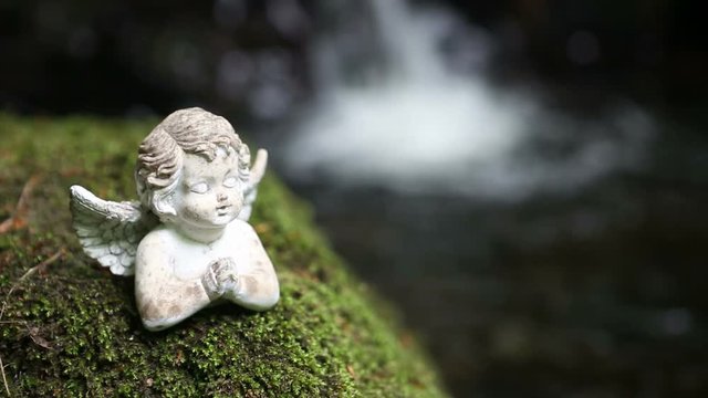 praying stone angel on moss in front of waterfall
