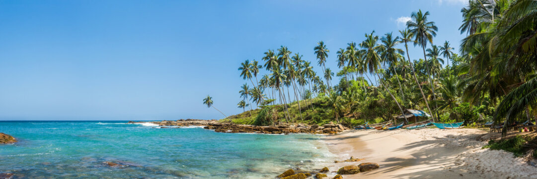 Panoramic view of the beach with the old tropical bungalow and traditional wooden fishing boats in Sri Lanka.