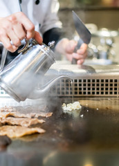 Hand of Chef cooking garlic on hot pan in front of customers.