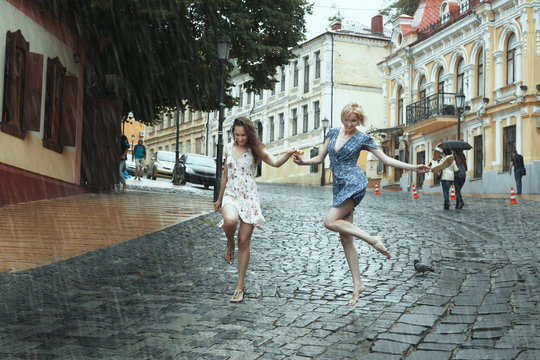 Women girlfriends stroll in the rain, they cheerfully jump.