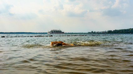 Man swimming in a lake with a boat in the background