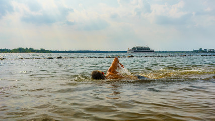 Man swimming in a lake with a boat in the background