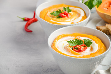 Pumpkin soup with cream and parsley on a grey concrete or stone background, selective focus, copy space