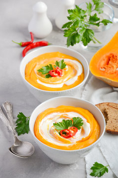 Pumpkin soup with cream and parsley on a grey concrete or stone background, selective focus
