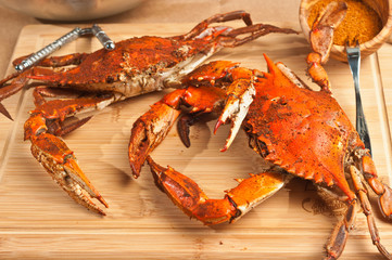 Pile of steamed and seasoned Chesapeake Bay blue claw crabs / on a wood cutting board with a steel cracker and a wood bowl of spicy,seasoning on brown paper table covering