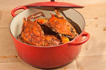 Pile of steamed and seasoned Chesapeake Bay blue claw crabs / on a wood cutting board with a steel cracker and a wood bowl of spicy,seasoning on brown paper table covering