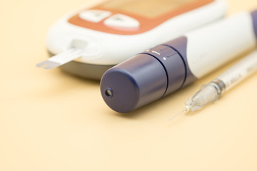 Close up of syringe for insulin and Glucose meter with lancet for check blood sugar level on orange background using as Medicine, diabetes, glycemia, health care and people concept