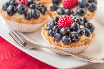 Tartlets with blueberries and raspberry on white plate.