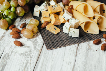 Assortment of cheeses with nuts and grapes on a white wooden background