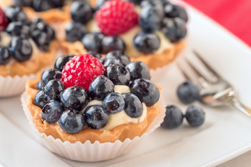 Tartlets with blueberries and raspberry on white plate.