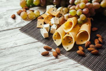 Assortment of cheeses with nuts and grapes on a white wooden background