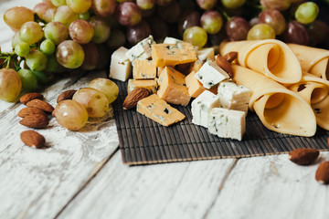Assortment of cheeses with nuts and grapes on a white wooden background