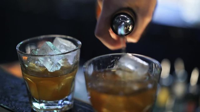 Close up of an unrecognizable bartender pouring a drink from a bottle into two shot cups. Handheld real time close up shot