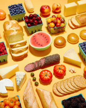 Picinic Spread of Farmers Market Fruits Vegetables Breads and Charcuterie in Grid Pattern on Yellow Background