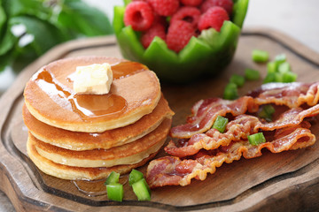 Tasty breakfast with pancakes, bacon and raspberry on wooden board