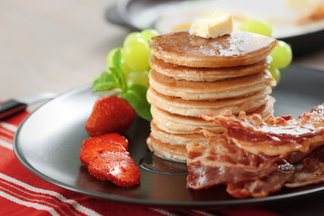 Tasty breakfast with pancakes, bacon and fruits on table