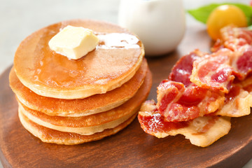 Pancakes with butter and bacon on wooden board