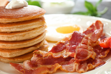 Tasty breakfast with pancakes, fried egg and bacon on table