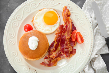 Tasty breakfast with pancakes, fried egg and bacon on table