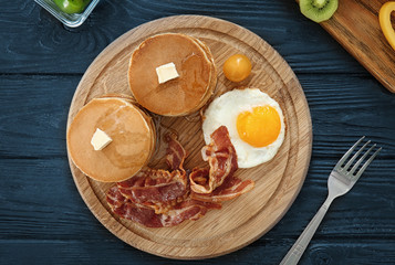 Tasty breakfast with pancakes, fried egg and bacon on wooden board