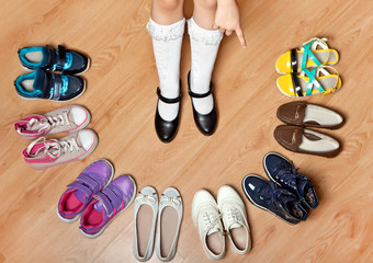 Girl in white socks and black shoes standing in a semicircle of different shoes.